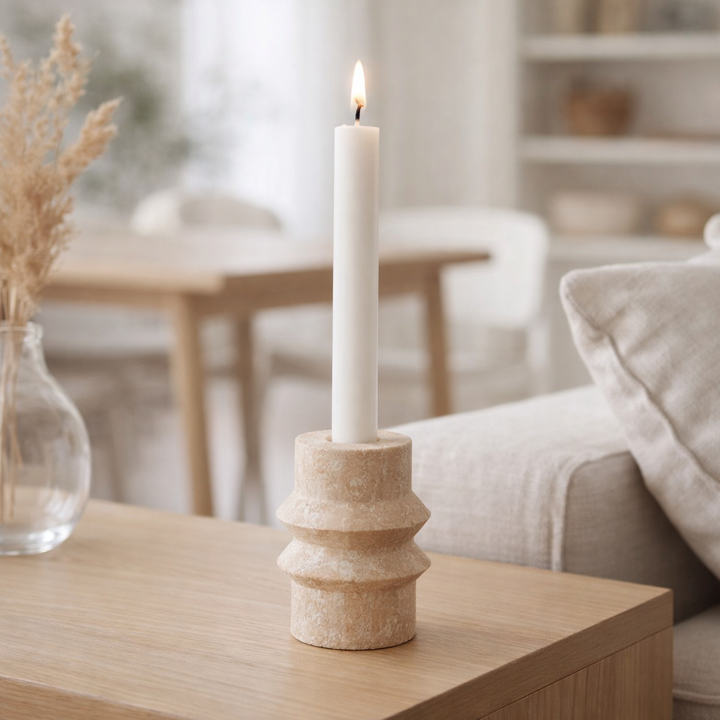 Bougeoir en travertin beige avec une chandelle allumée sur une table basse en bois
