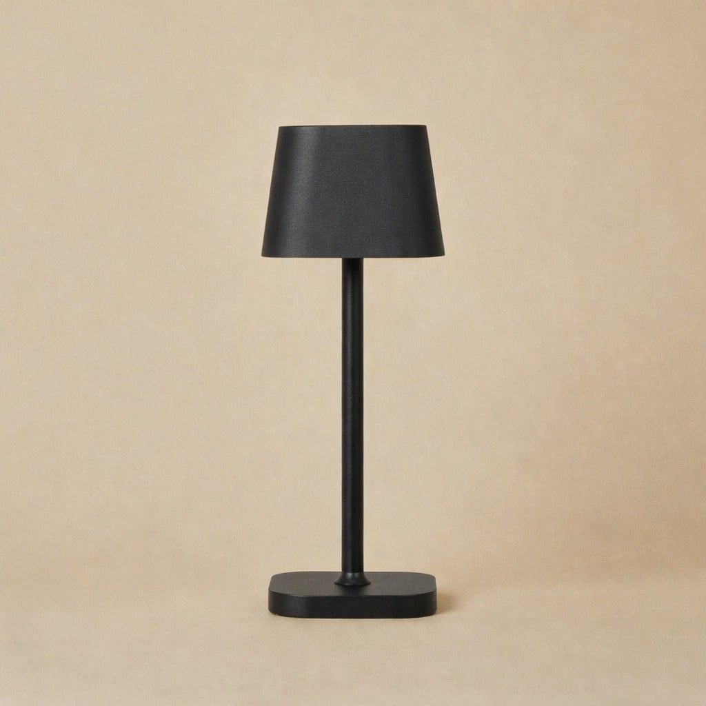 Lampe de table rechargeable noire Ava allumée sur un meuble