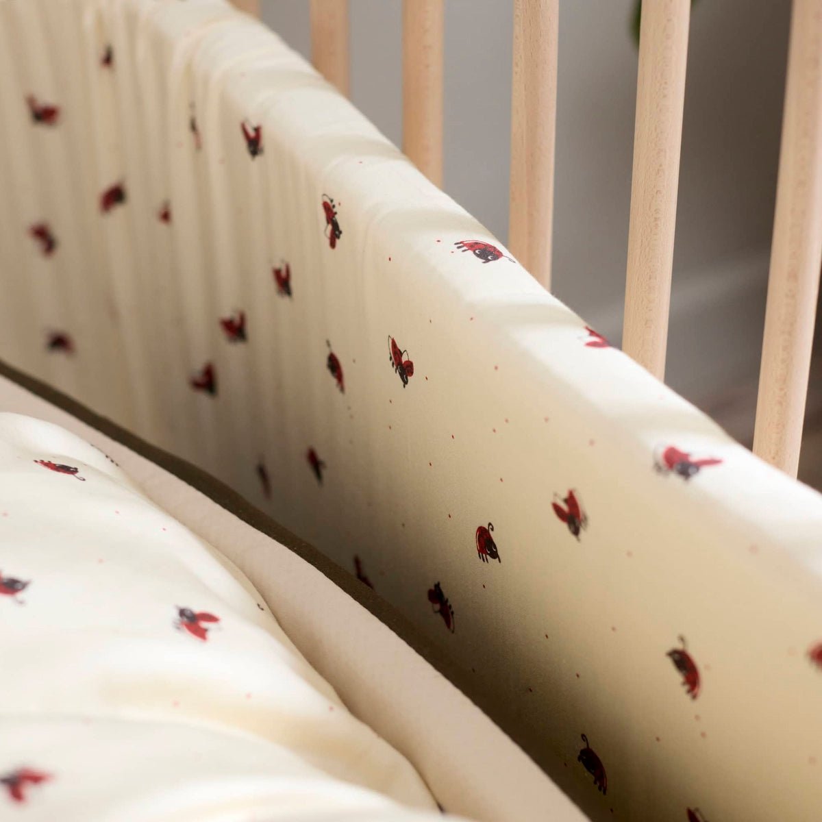 Tour de lit Lucky OYOY Living Design avec motif coléoptère rouge sur fond blanc cassé.