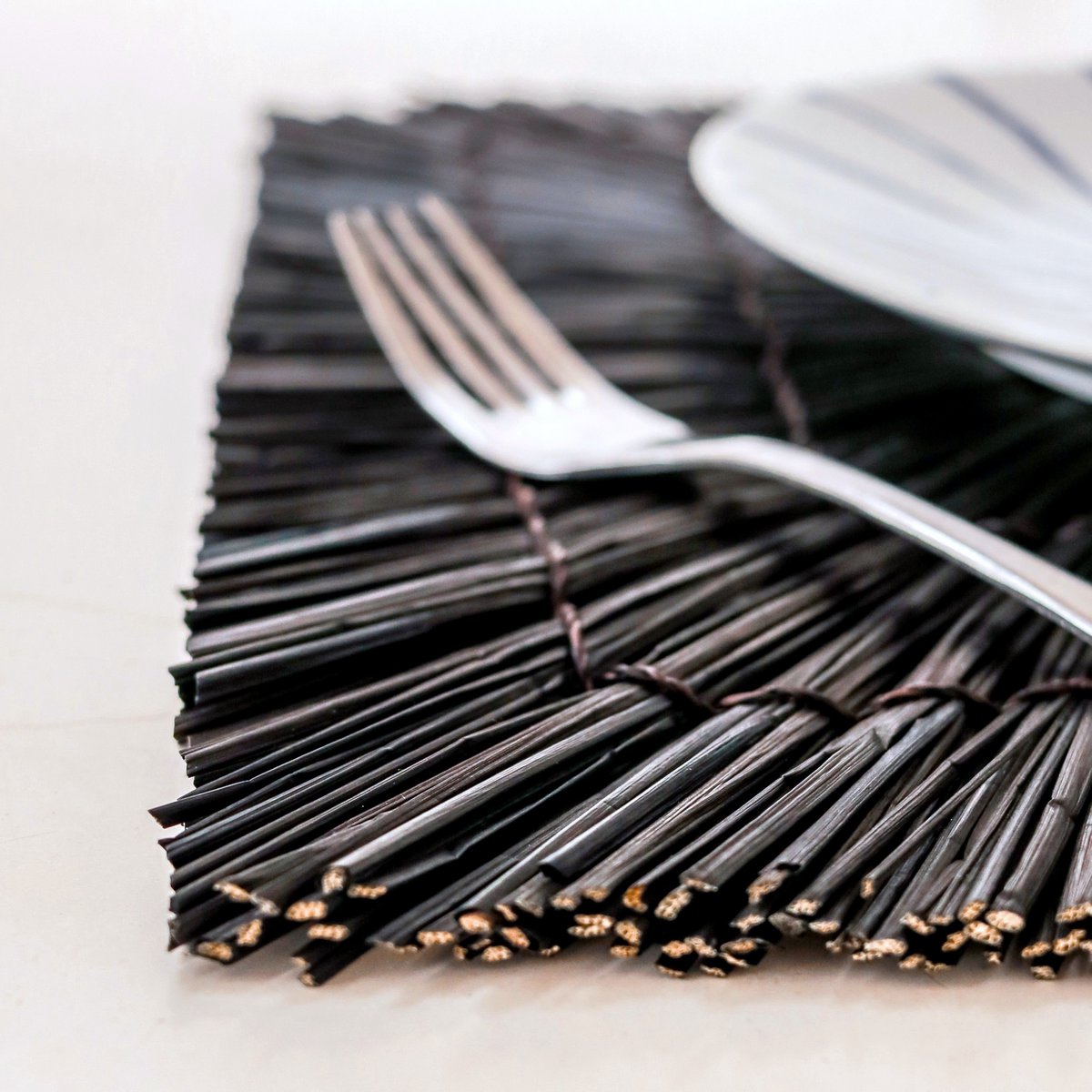 Set de table carré Varna en jonc de mer noir sur une table élégante.