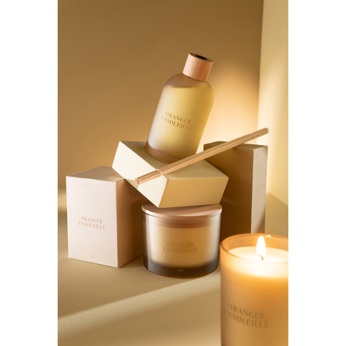 Bougie parfumée J-Line Oranger Ensoleillé, en train de brûler, diffusant une lumière douce.
