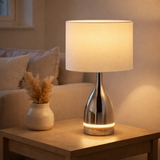 La lampe de table LED Cosima mesure 43,5 cm de haut, parapluie Ø 25 cm, en métal, en plastique, matériau textile dans les couleurs chrome et blanc. Les deux LED intégrés dans le pied léger et la version E14 en situation